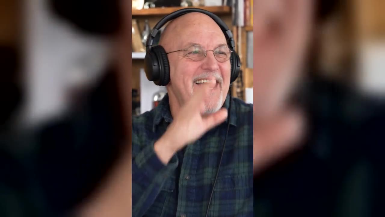 An Outstanding Tiny Desk AI video: a laughing man in headphones in front of bookshelves